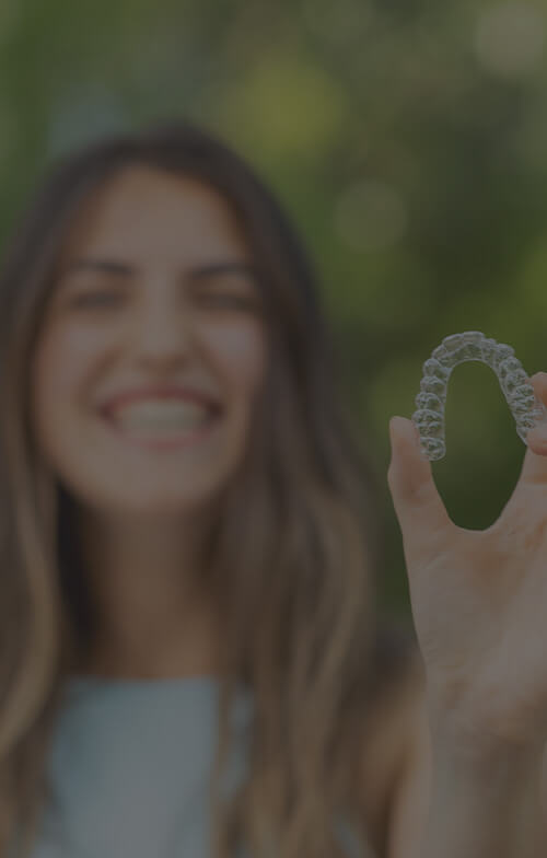 Woman holding up clear aligners - Orthodontics in Denver and Parker, CO